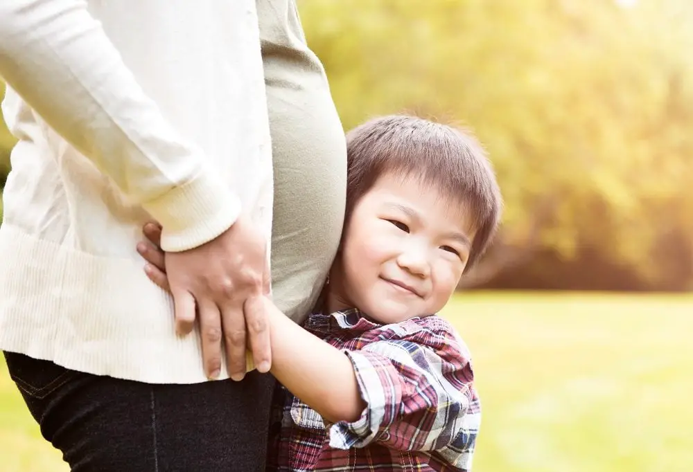 A shot of an Asian boy kissing the belly of his pregnant mother