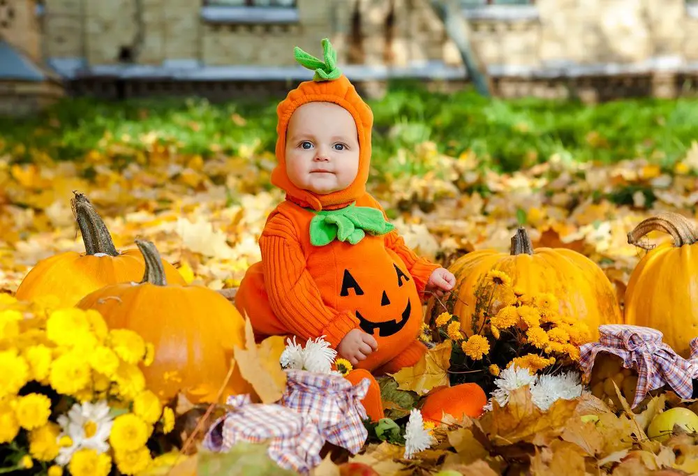 Child In Pumpkin Suit On Background Of Autumn Leaves
