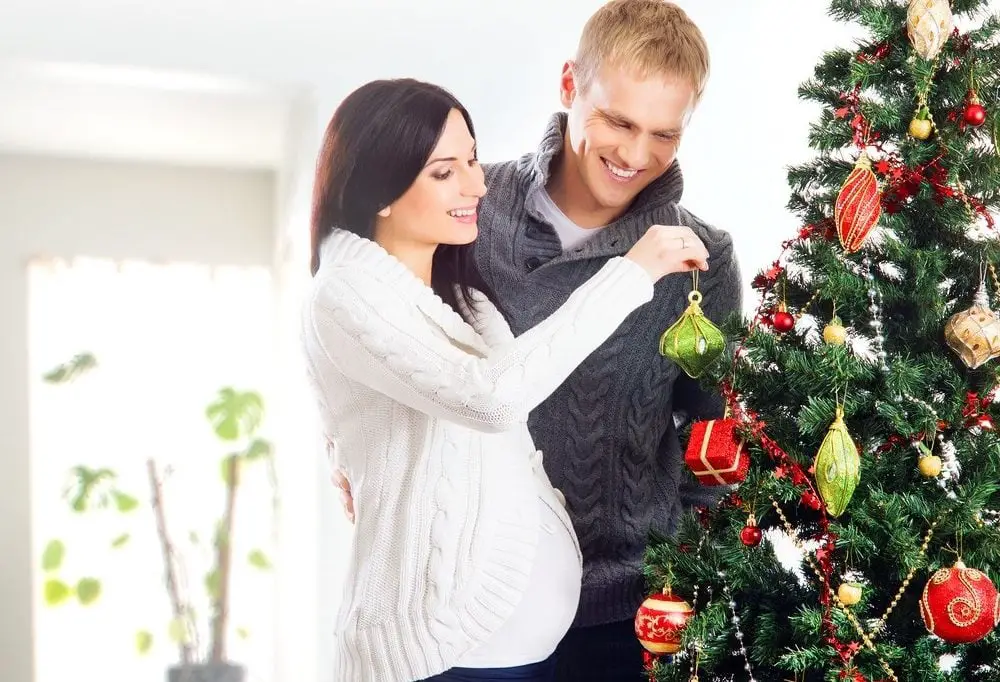 Young pregnant woman and happy father decorating Christmas tree
